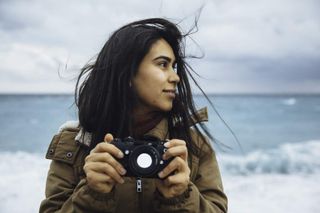 Female photographer holding a camera by crashing waves