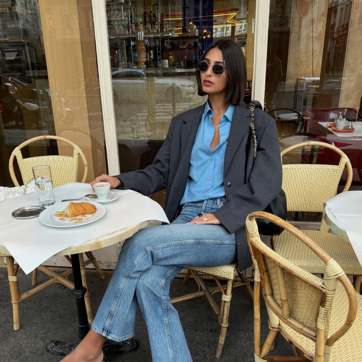 A French woman sitting outside of a cafe eating a croissant and drinking a coffee