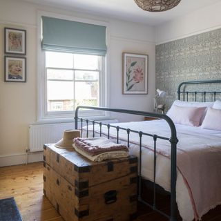 White bedroom with metal hospital bed, pink bedding, duck egg blind, William Morris wallpaper, wooden chest