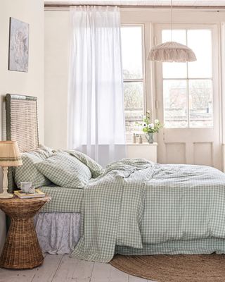 A bedroom with neutral walls, a woven sided table, and green gingham bedsheets