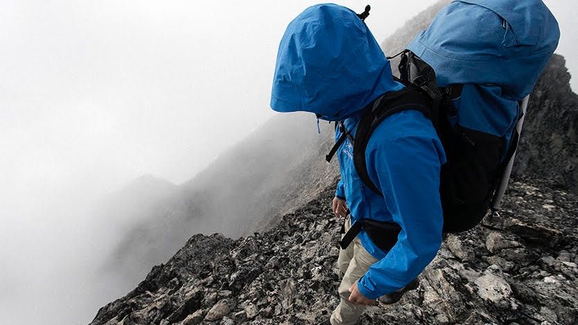 Best hiking backpacks: a man wearing a blue waterproof jacket hikes down a steep mountain