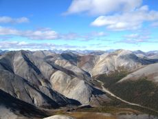 Plate tectonics is the means through which mountains are formed. Image shows rippled gray mountains, mostly treeless, beneath a cloud-studded blue sky. The Baird Mountains in Alaska’s Kobuk Valley National Park formed when two tectonic plates along a convergent boundary collided, causing solid rock to buckle and fold.