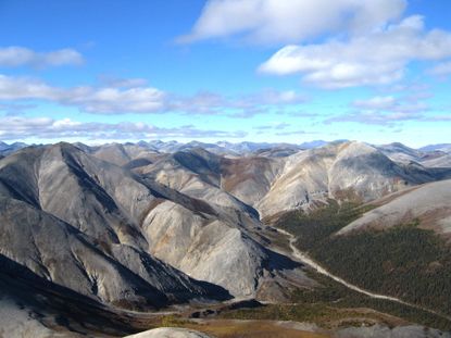 Plate tectonics is the means through which mountains are formed. Image shows rippled gray mountains, mostly treeless, beneath a cloud-studded blue sky. The Baird Mountains in Alaska&rsquo;s Kobuk Valley National Park formed when two tectonic plates along a convergent boundary collided, causing solid rock to buckle and fold.