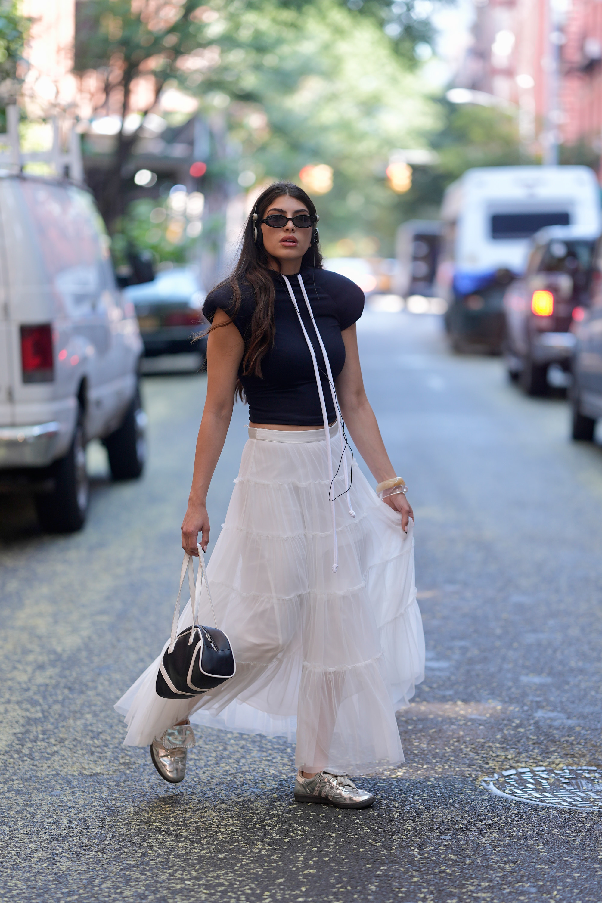 NEW YORK, NEW YORK - JULY 30: Maya Adele is seen wearing a Yori Sport navy top, white maxi skirt, adidas by Wales Bonner silver samba sneakers, black sunglasses, vintage headphones and holding a navy and white purse on July 30, 2025 in New York City. (Photo by 305pics/GC Images)