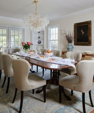 neutral dining room with off white linen dining chairs, wooden oval table, antique painting and globe chandelier