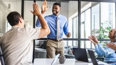 Upbeat boardroom environment with happy executives clapping while two male colleagues high five each other.