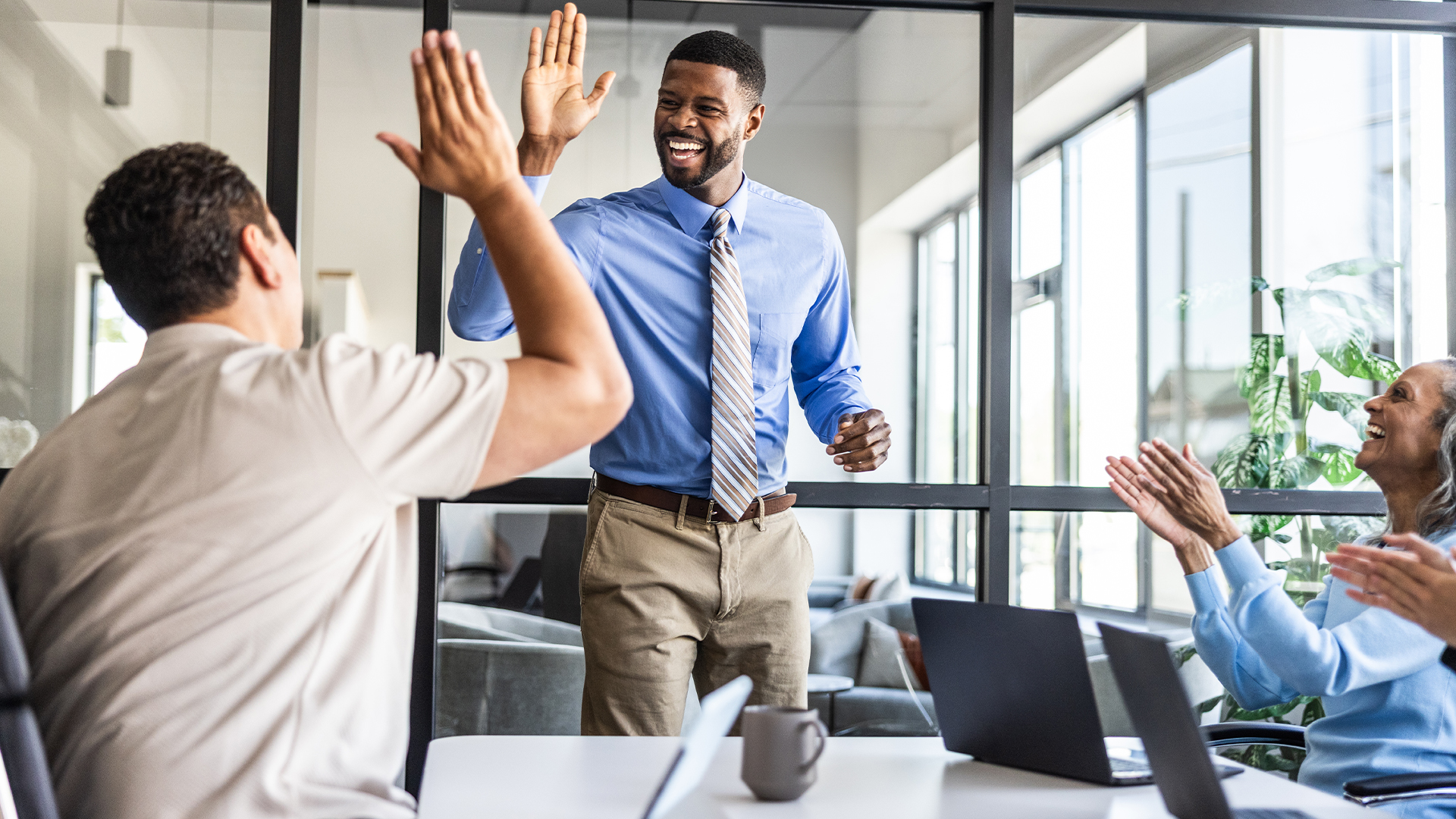 Upbeat boardroom environment with happy executives clapping while two male colleagues high five each other.