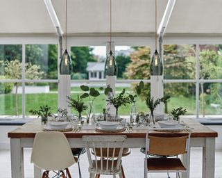 White dining area by Fritz Fryer with smoked glass pendant lights and assorted chairs with distressed dining table