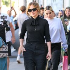 Jennifer Lopez in LA wearing black sunglasses, a black sweater, black cropped trousers, and black lace-up ballet flats.