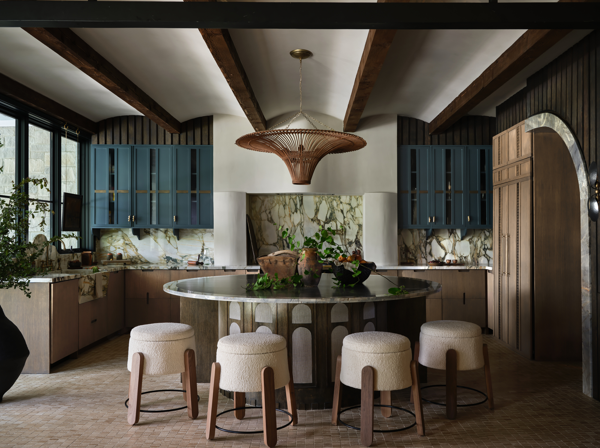 A modern kitchen with a circular dining table, boucle bar stools, and small-format tile flooring in a warm grey tone