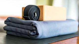 Yoga block and strap sitting on blanket on top of yoga mat on wooden floor in studio