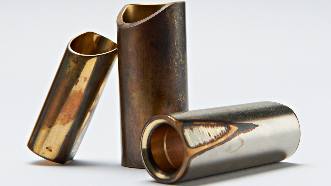 Three brass guitar slides on a white background