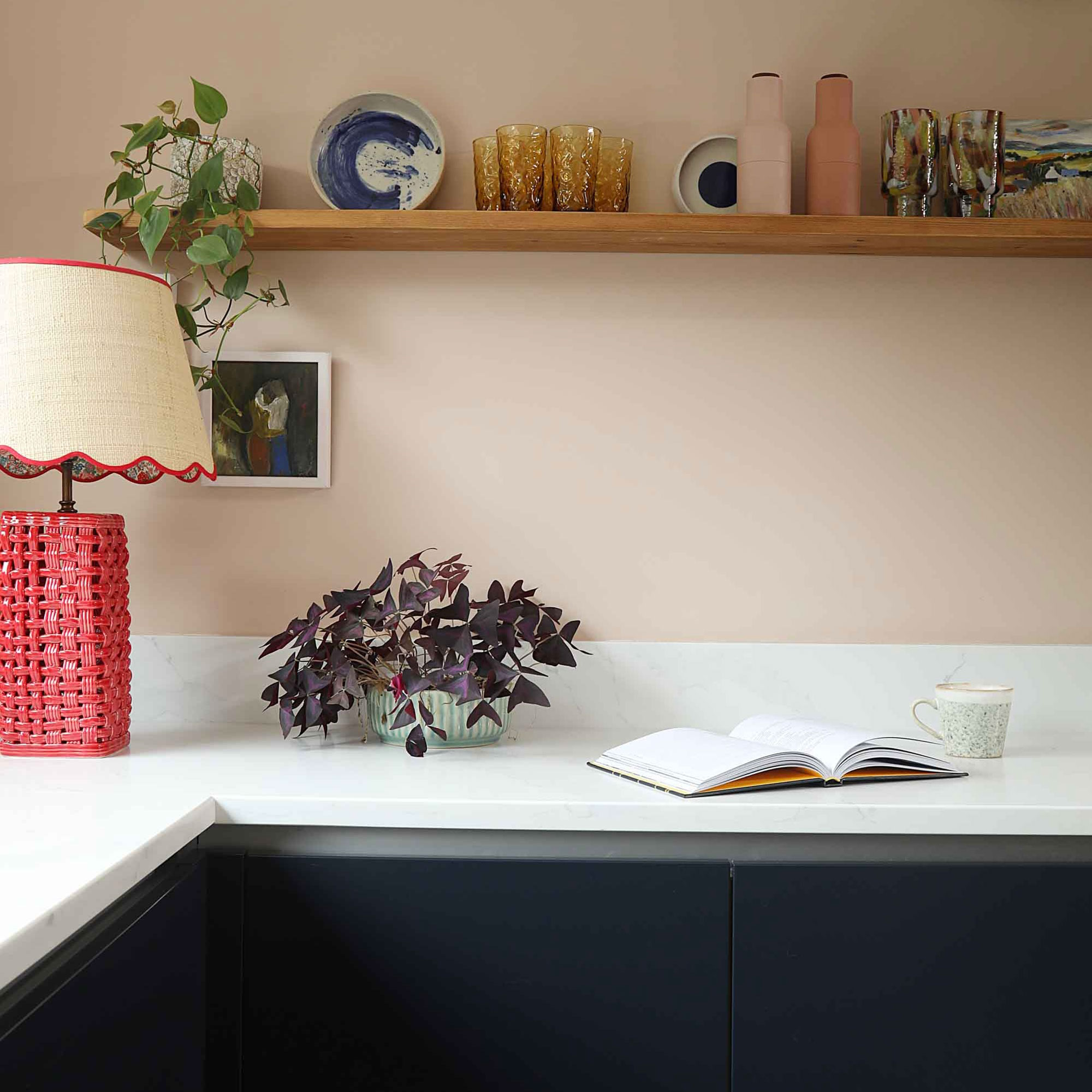 Marble kitchen work top with open book, houseplant and woven red table lamp