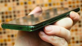 OnePlus 12 holdes opp fra en vinkel for å vise skjermen og bunnen av telefonen.