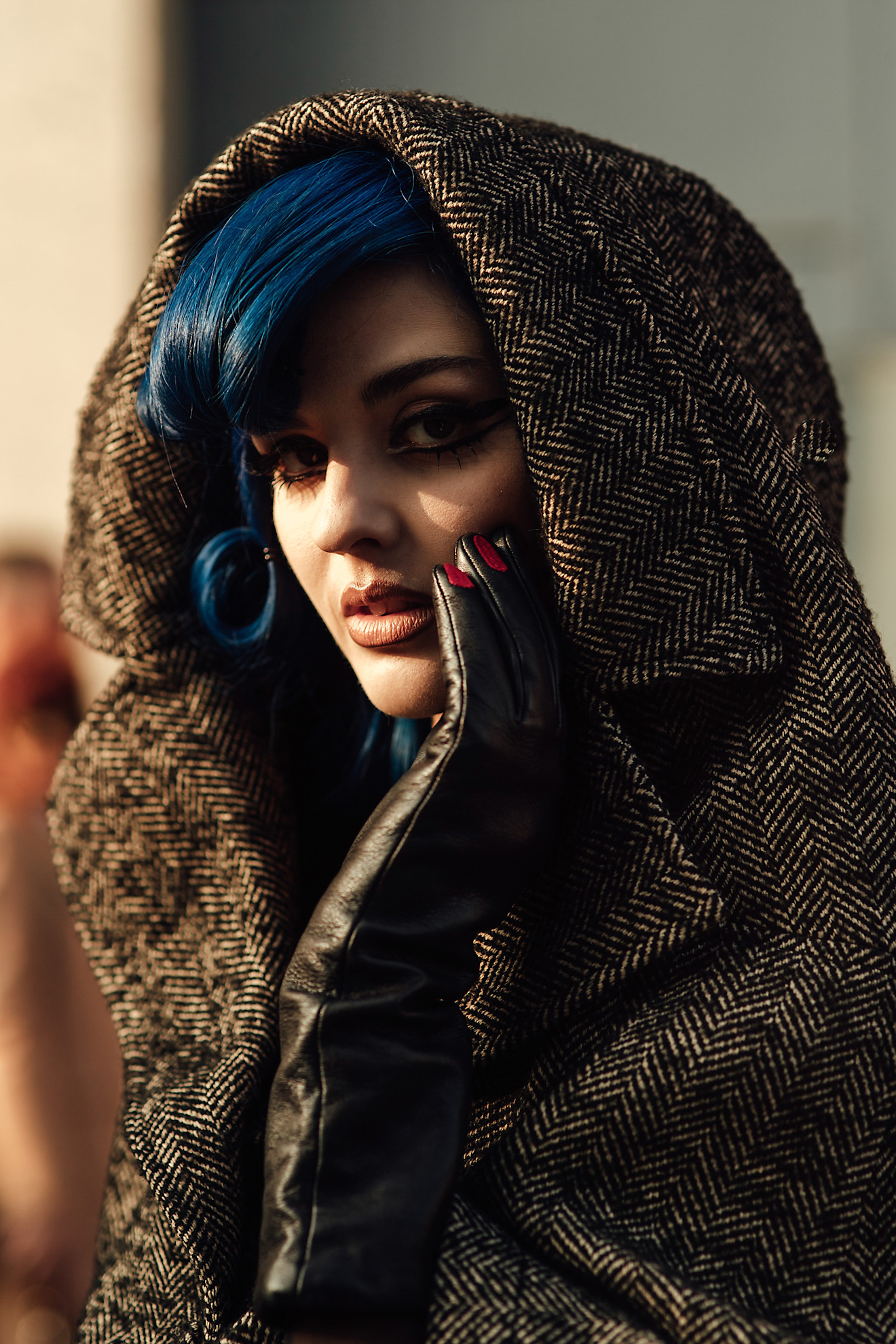a woman in a tweed coat with blue hair and bold brows