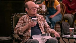 Kurtwood Smith in That '90s show with a newspaper in his lap, he's holding a coffee cup in his left hand and he's looking over his glasses. 