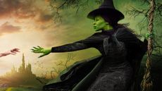 A green witch extends her arm out to reach for another hand while holding a broomstick 