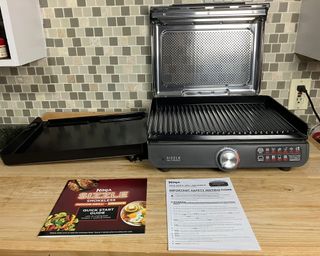 Ninja Sizzle smokeless indoor grill and griddle on wood effect countertop with full-color instruction manual