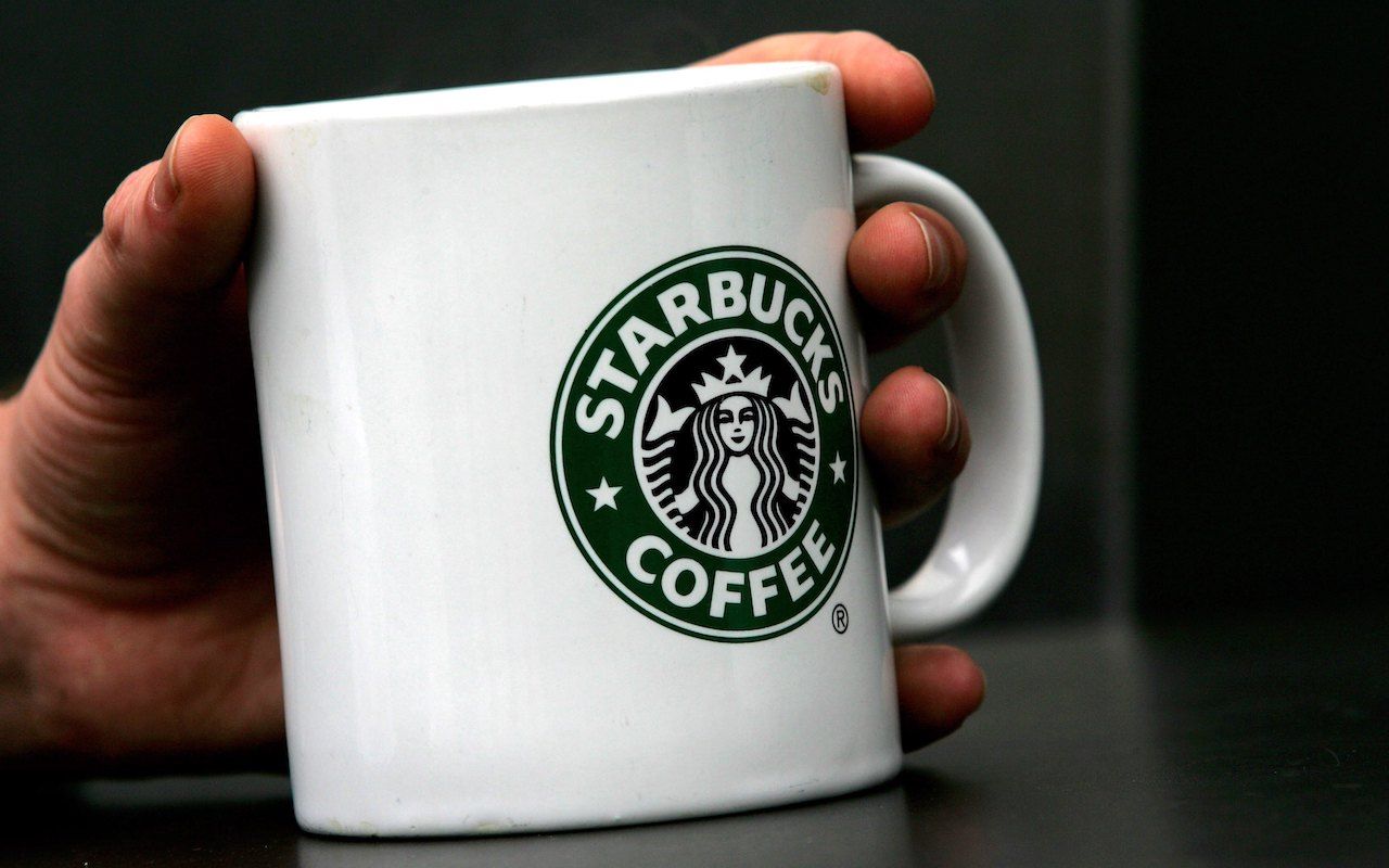 LONDON - APRIL 25:A man holds Starbucks Coffee mug in central London on April 25, 2006 in London, England. The all traditional English style Breakfast &amp;#039;Fry-Up&amp;#039;is under threat of being replace