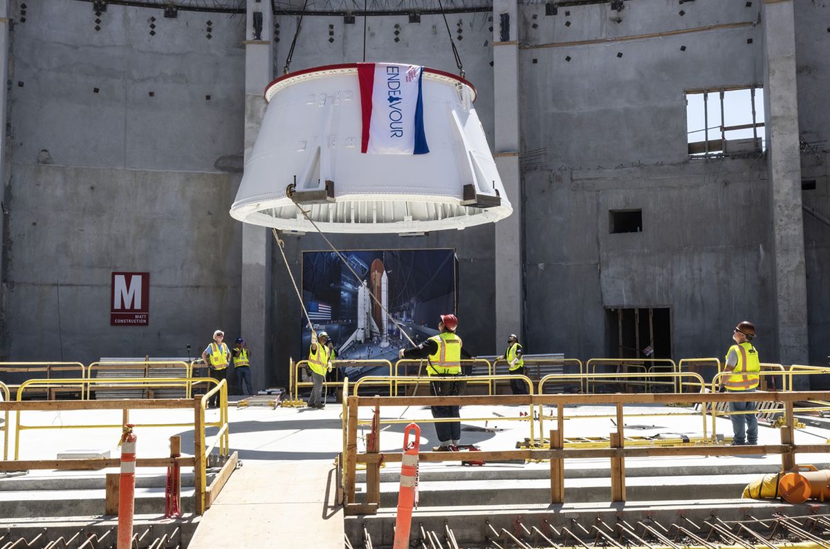 workers in yellow vests guide part of a white solid rocket booster to the floor