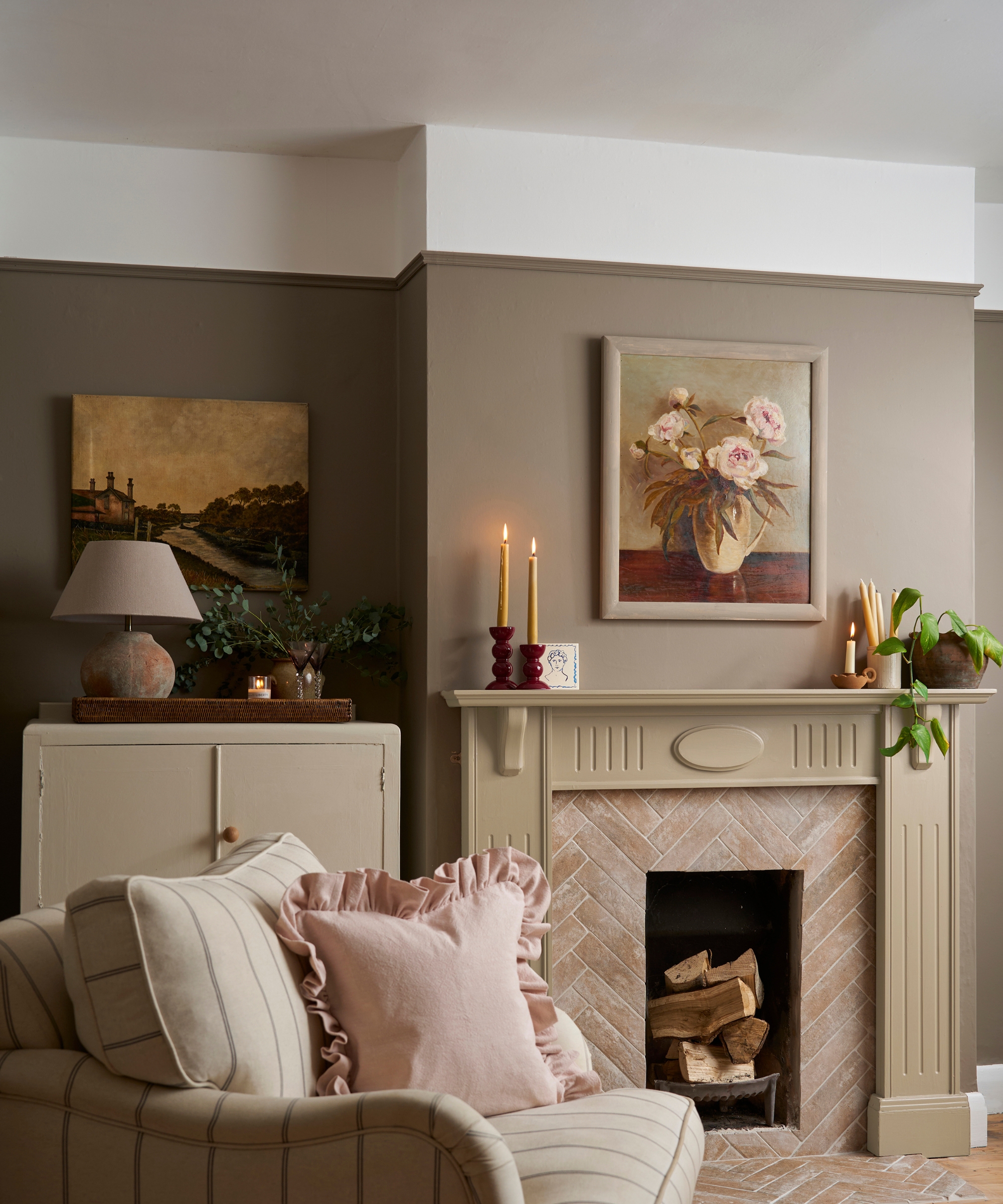 Two-tone taupe living room with fireplace, floral painting, cabinet, and a sofa with pink ruffled cushion.