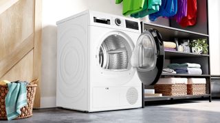 tumble dryer with door open in utility type rom with colourful clothing hanging