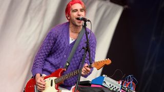 Carlos O'Connell wears a purple cardigan and plays a red Fender Mustang live at Reading Festival 2024