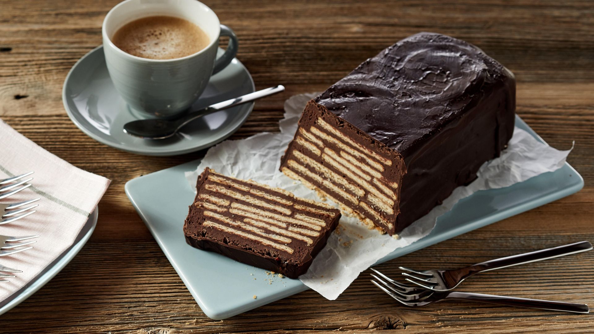 A slice is cut from a chocolate biscuit cake log served with a cup of tea