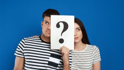 Couple holding question mark sign on blue background