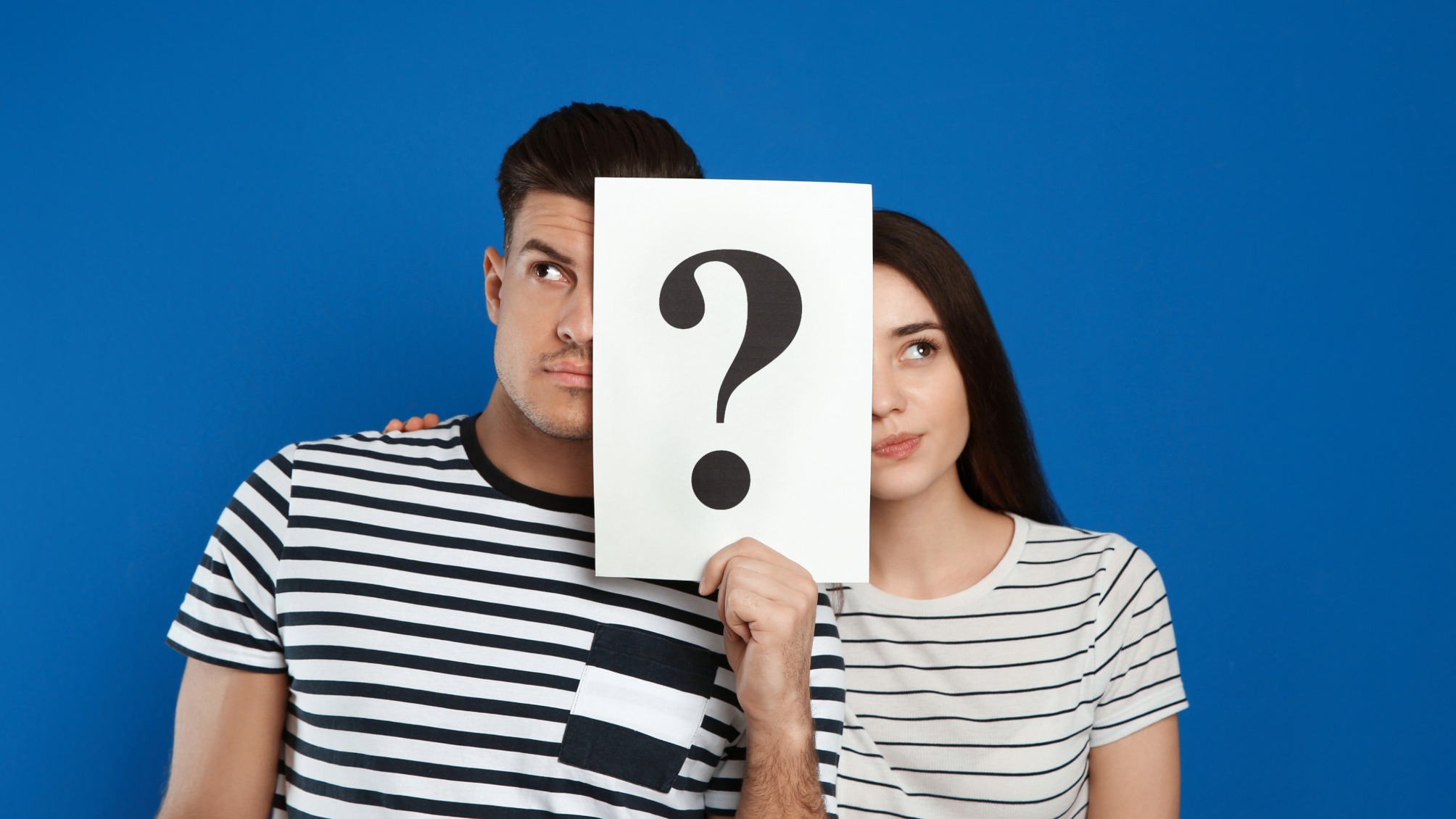Couple holding question mark sign on blue background