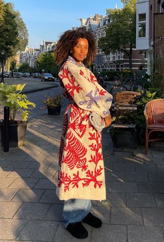 quilted patchwork jacket trend is shown on a woman in the street wearing a long coat with jeans and clogs