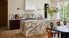 modern kitchen with timber floors, marble counter and backsplash, dark cabinets, and a dining table with antique-looking chairs