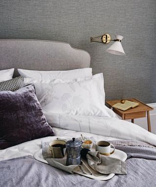 A bedroom with textured wallpaper, angled wall light, and a double bed with a breakfast tray.