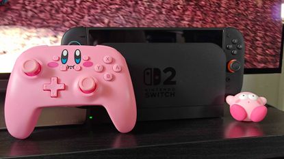 PowerA Kirby mouthful controller next to Switch 2 on black TV unit.