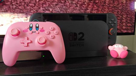 PowerA Kirby mouthful controller next to Switch 2 on black TV unit.