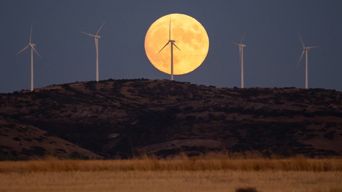 The full Harvest Moon rises over wind turbines of a wind farm with a recently harvested wheat field bellow.
