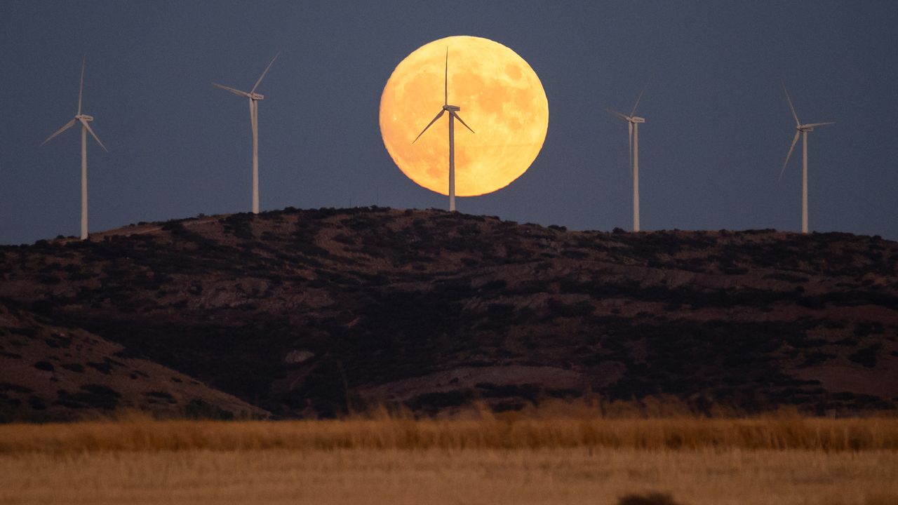 The full Harvest Moon rises over wind turbines of a wind farm with a recently harvested wheat field bellow.