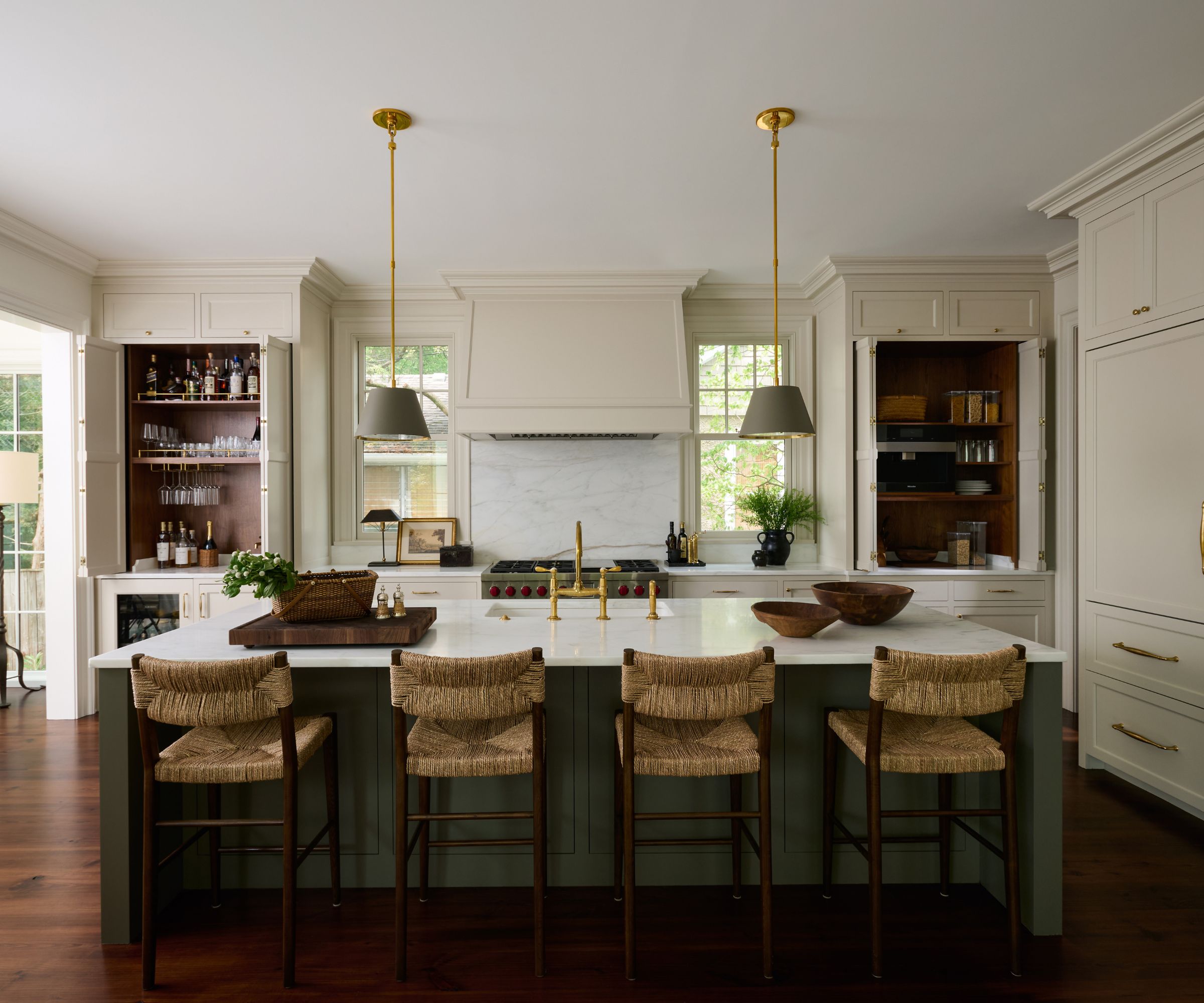 A large kitchen with creamy white cabinets, dark wood flooring, a large island painted dark green with a white countertop, and four woven bar seats.