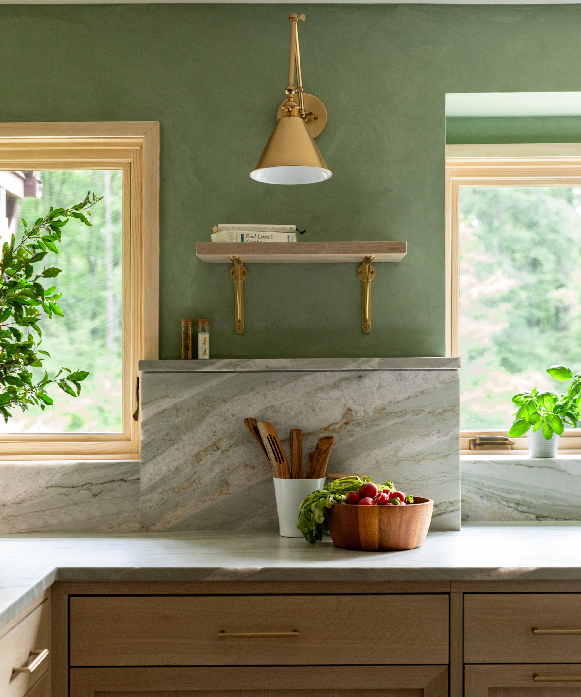 Marble kitchen countertop with wooden drawers, sage green painted walls and gold sconce with shelf underneath