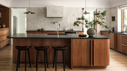 A large kitchen with cherry wood cabinets and island, black countertops, and neutral square zellige wall tiles