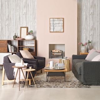 a neutral living room with whitewashed wood panel walls, a pink chimney brest, dark grey and blue sofa and armchair set, wooden furniture and mozaic rug
