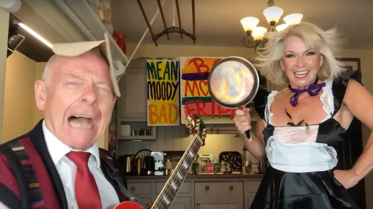 Robert Fripp and Toyah Willcox in the kitchen. Robert has a pancake on his head while Toyah brandishes a frying pan