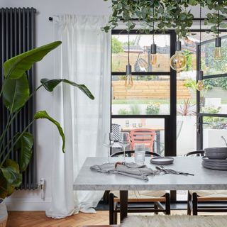 dining area with plants, table and bench seating, and French doors overlooking patio and garden