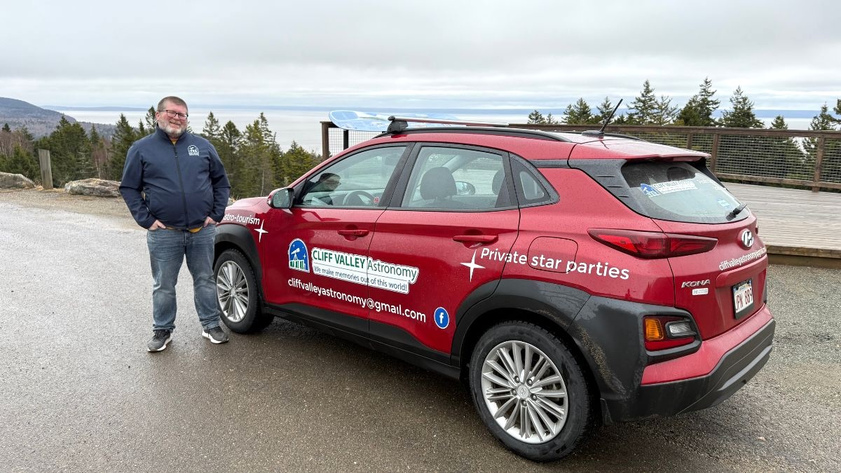 A person stands next to a Red Compact Car in Canada