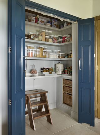 A built in walk in pantry with shelving and blue folding doors