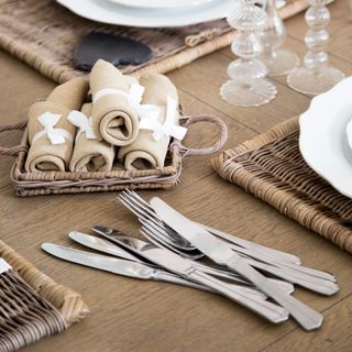 Wooden table with pile of cutlery and napkins in woven basket