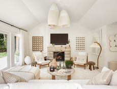 White living room with stone fireplace, white chaise sofa, white and wood armchairs, terrazzo top coffee table, trio of suspended lights and an indoor tree