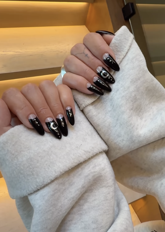 a person wearing a black half moon manicure with silver designs