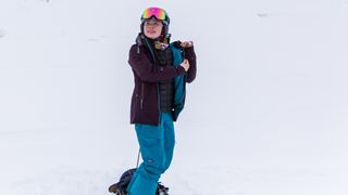 A woman wearing a Patagonia Women’s Storm Shift Jacket holds the front open to show the inner fabric, standing on a snowy mountainside.
