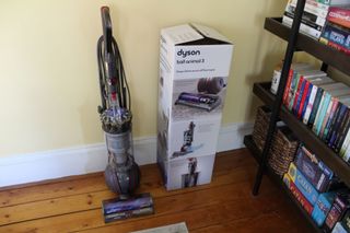 Dyson Ball Animal 3 and its original packaging on wooden floor next to shelves in Camryn's home